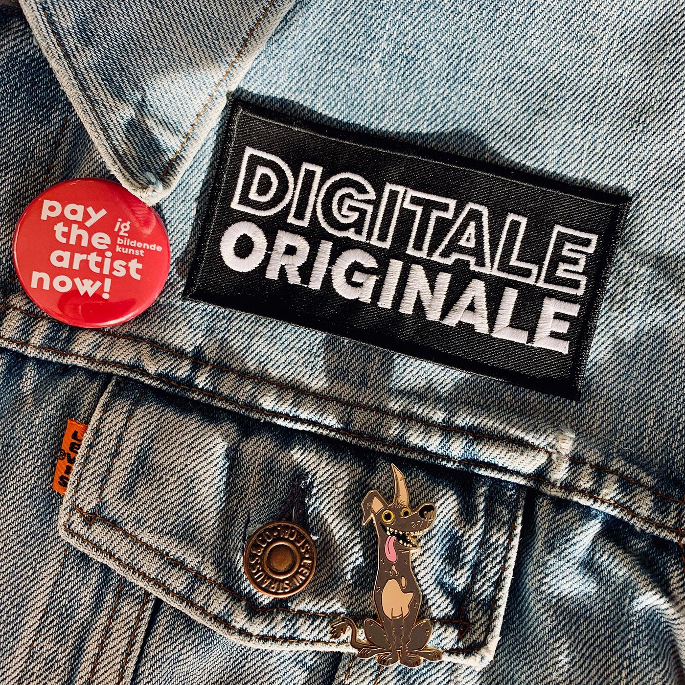 Digitale Originale Podcast Keyvisual: Nahaufnahme Jeansjacke - Aufnäher Patch "DIGITALE ORIGINALE", Nadelbutton "pay the artist now!", Hund-Ansteckpin